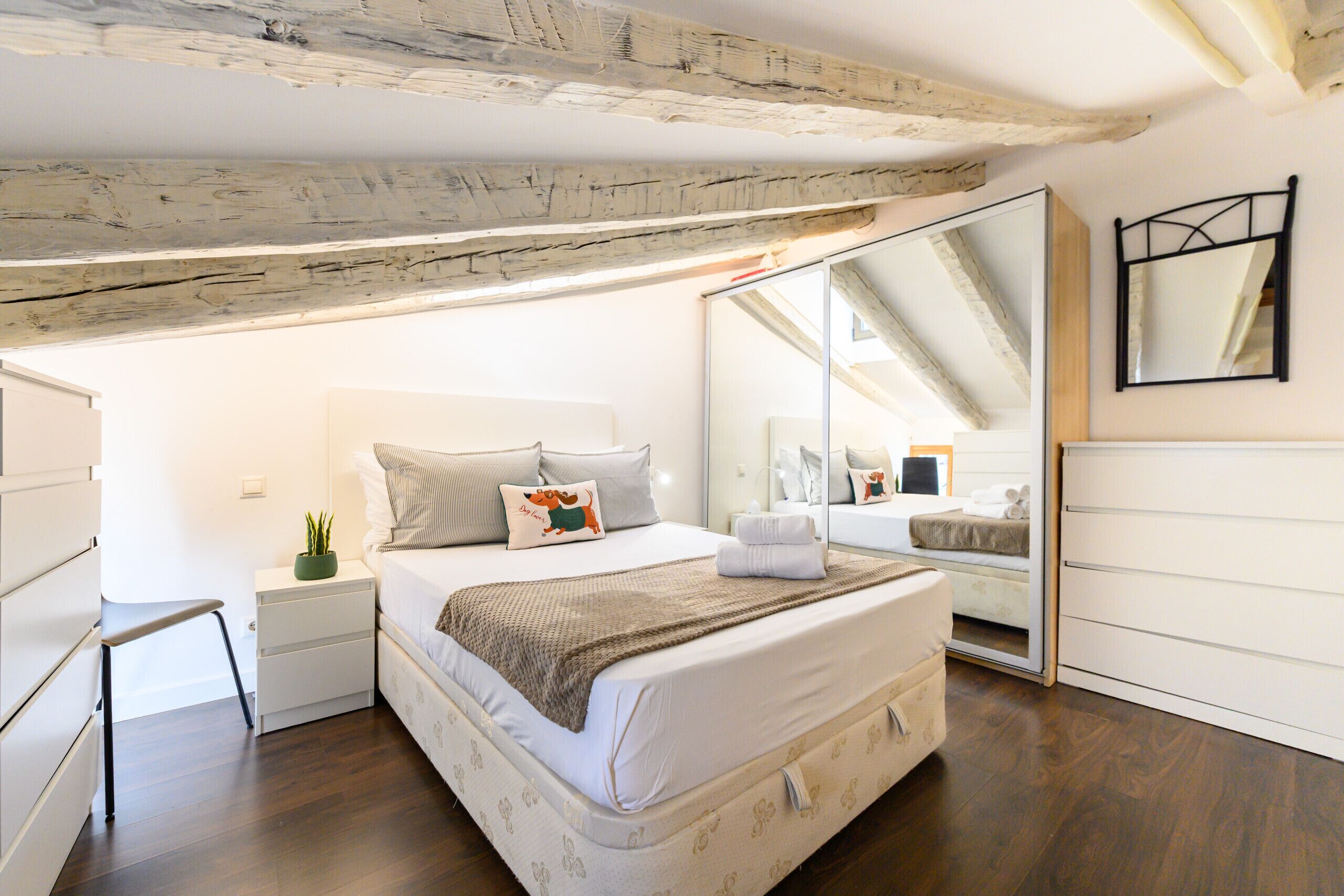 Une chambre à coucher avec un grand lit, une table de chevet, un miroir et une plante en pot.