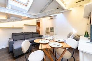 Ein modernes Wohnzimmer mit einer Couch, einem Esstisch und Stühlen. Ein Fenster bietet Blick auf den Himmel.