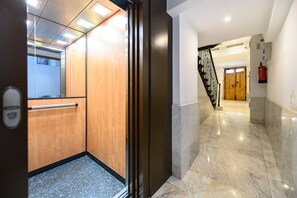 Eine Hotelhalle mit Marmorboden, einem Holzelevator und einer Treppe zu einem weiteren Raum.