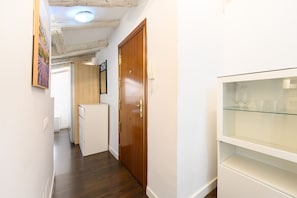 A narrow hallway with a wooden door, a small refrigerator, and a glass shelf with glasses.