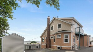 Een twee verdiepingen tellend huis met een grote schoorsteen, een garage en een kleine tuinhuis.