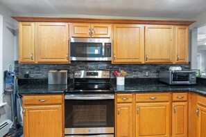 A kitchen with wooden cabinets, a stainless steel refrigerator, a microwave, an oven, and a toaster. - The Nahant Perch: ocean view, walk to beach (Nahant)