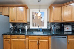 A kitchen with wooden cabinets, a granite countertop, a stainless steel sink, and a dishwasher. - The Nahant Perch: ocean view, walk to beach (Nahant)
