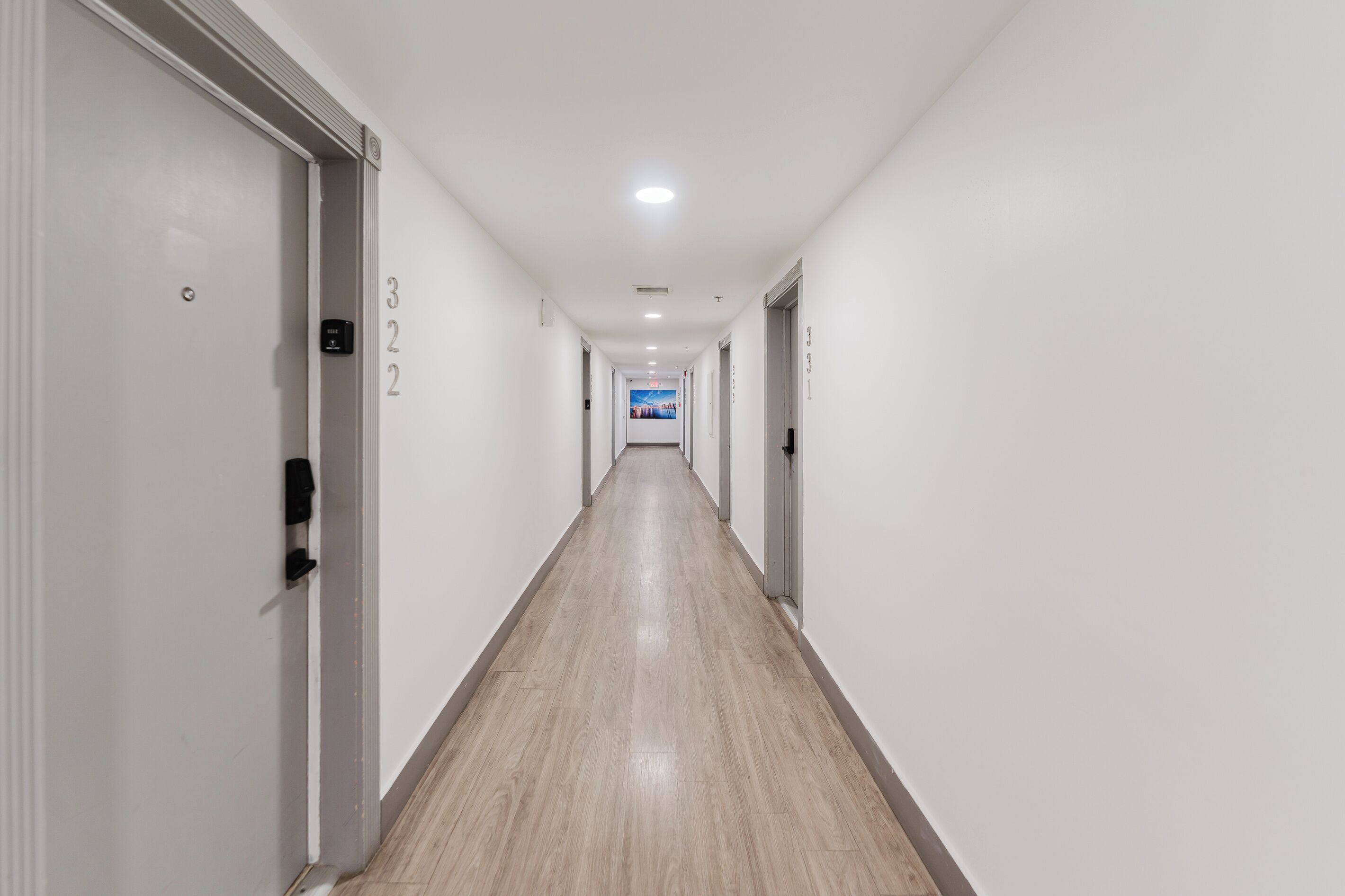 A long, narrow hotel corridor with white walls and wooden flooring.