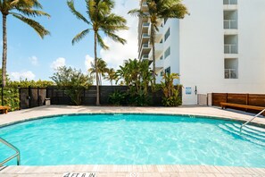 A swimming pool with a wooden deck, surrounded by palm trees and a building with balconies. - SoFi Ocean Drive Villa | Direct Beach Access (Miami)