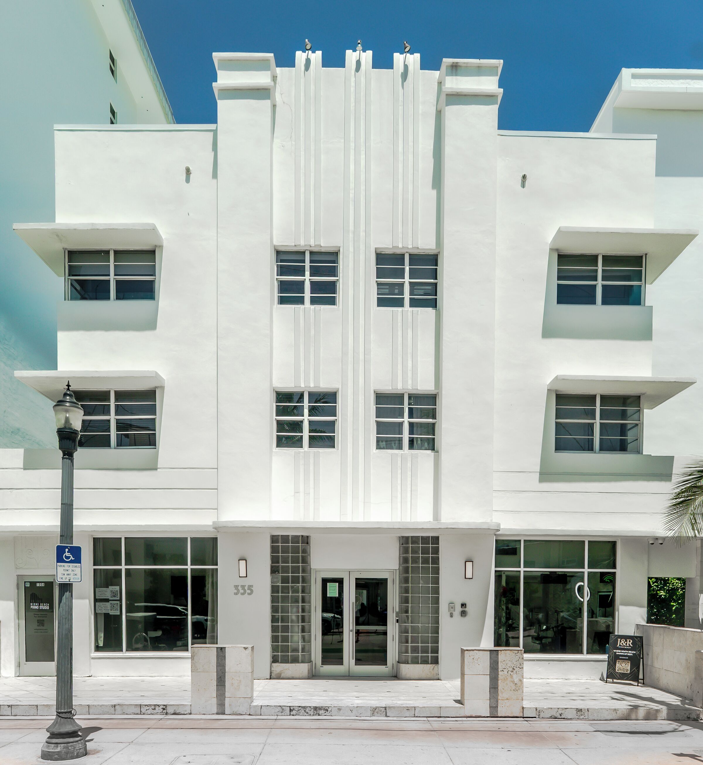 Un edificio blanco con múltiples ventanas y una puerta, número 335, con un letrero de estacionamiento y un cartel con código QR en la acera.