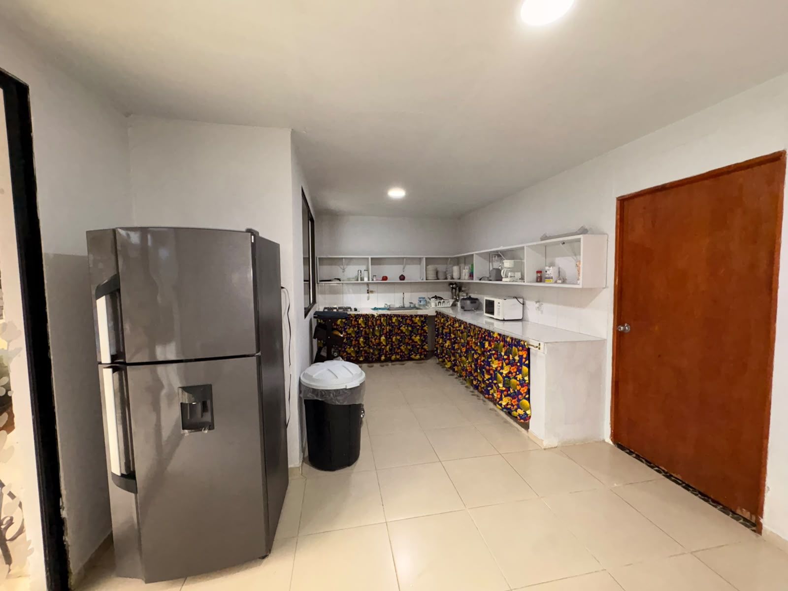 Una cocina con refrigerador, contenedor de basura y microondas.