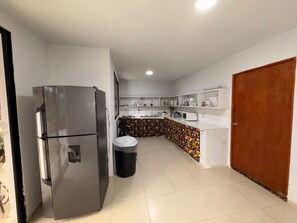 A kitchen with a refrigerator, a trash bin, and a microwave.