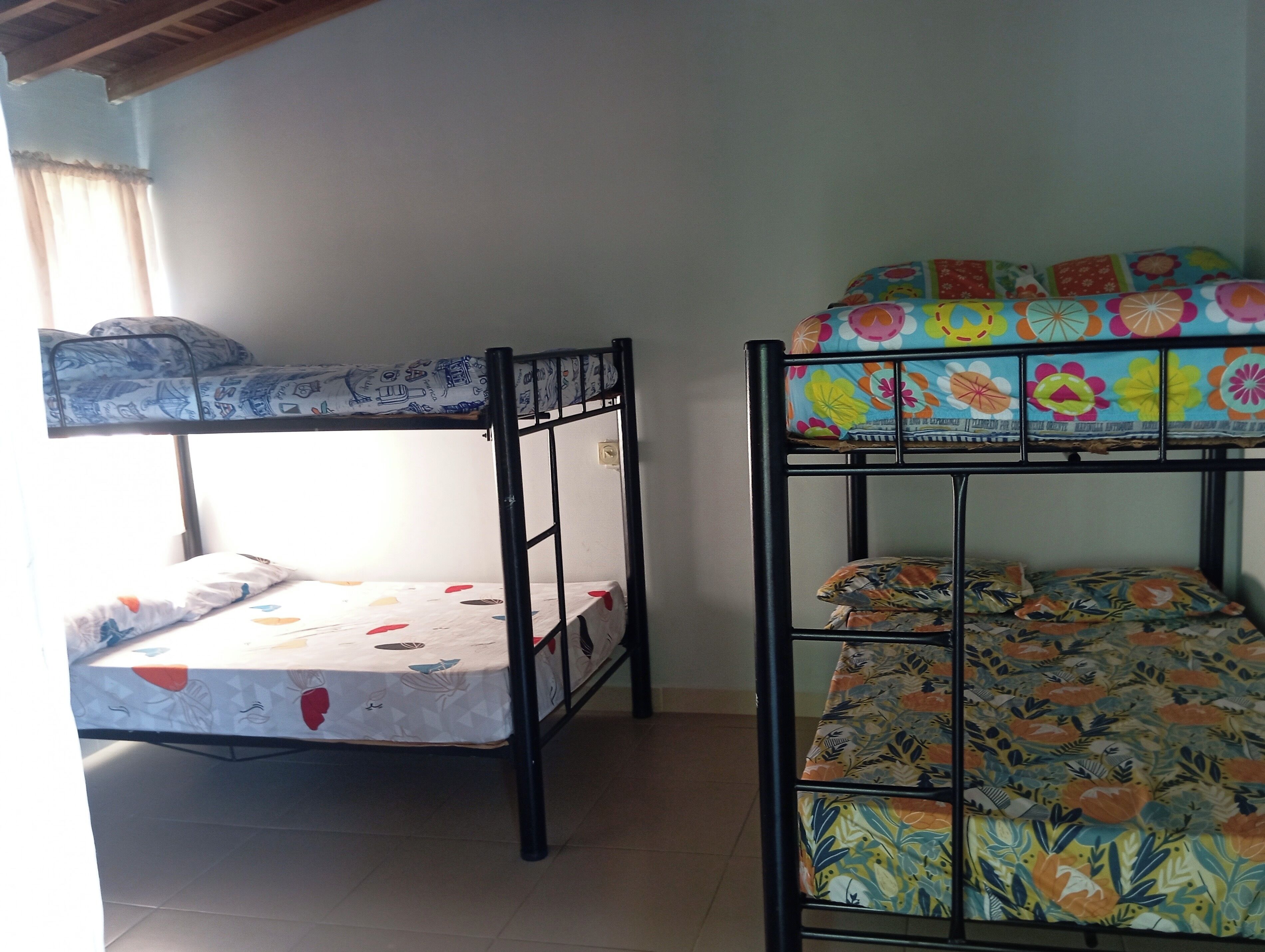 Two bunk beds with colorful bedding, a window with curtains, and a tiled floor.