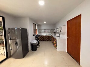 A kitchen with a refrigerator, a trash bin, and a tiled floor.
