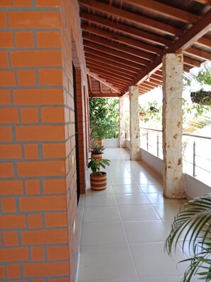 A covered corridor with tiled flooring, brick walls, and columns supporting the roof.