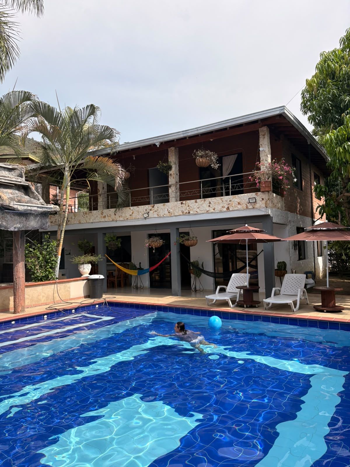 Una casa de dos pisos con piscina, mobiliario exterior y plantas en macetas.