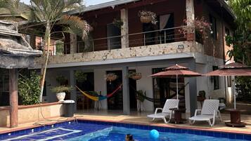 Una casa de dos pisos con piscina, mobiliario exterior y plantas en macetas.