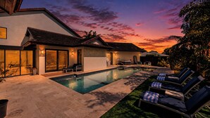 Ein modernes Haus mit Swimmingpool, Sitzgelegenheiten im Freien und einem Sonnenuntergangshimmel.