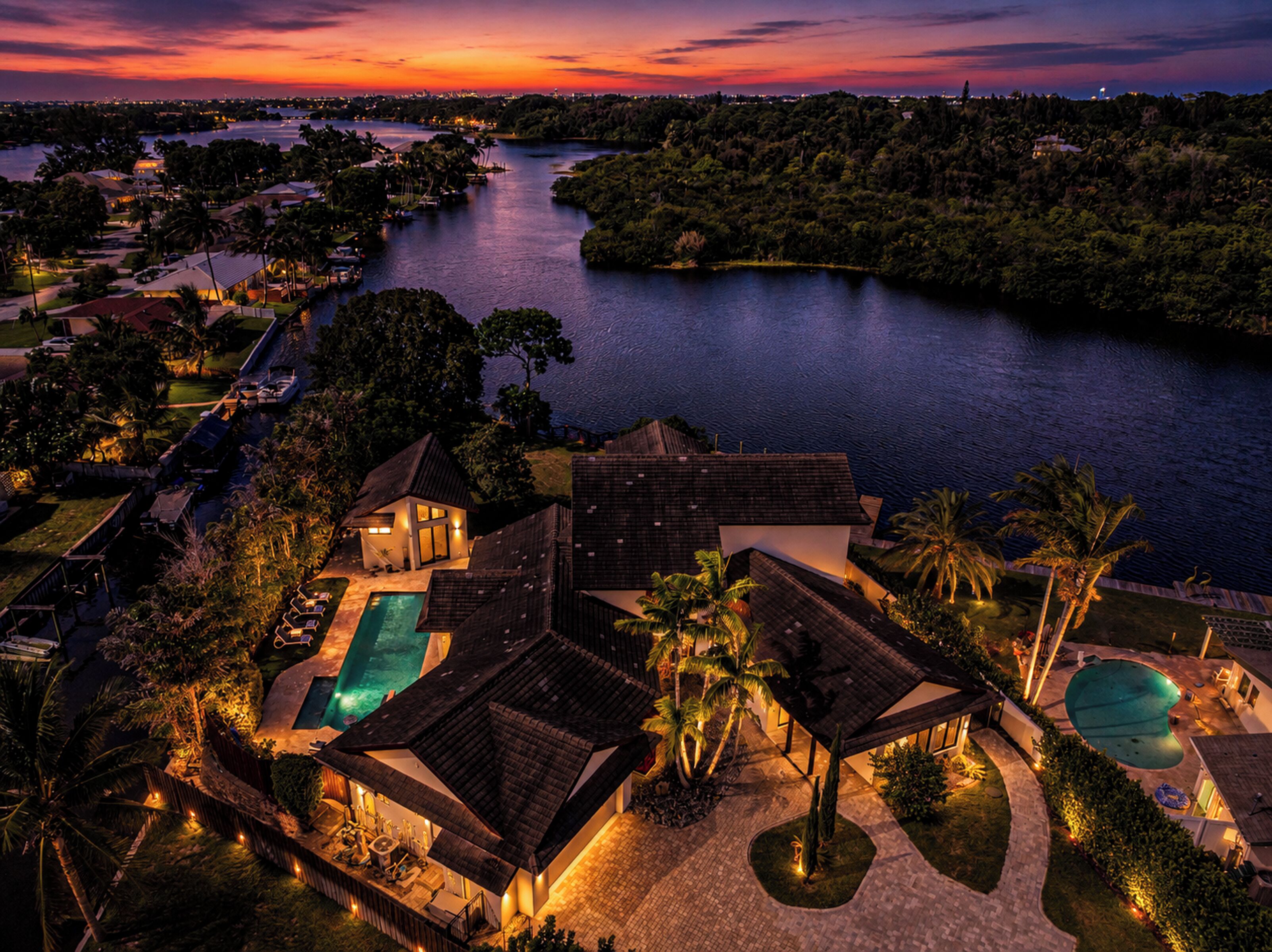 A large house with a swimming pool, surrounded by lush greenery and a view of a river.