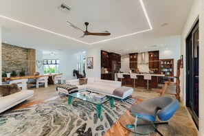 A modern living room with a sofa, coffee table, and a dining area with a wooden table and chairs. - Waterfront Luxe Smart Home | Pool | Gym | Spa (Lantana)