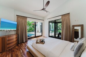 Ein Hotelzimmer mit Bett, Fernseher, Deckenventilator und Blick auf Pool und Strand.