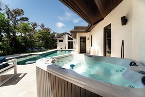 Ein moderner Poolbereich im Freien mit Whirlpool, Liegestühlen und einer überdachten Terrasse.