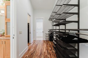 A hallway with wooden flooring, a kitchen area with white cabinets, and a black metal rack with hangers. - Waterfront Luxe Smart Home | Pool | Gym | Spa (Lantana)
