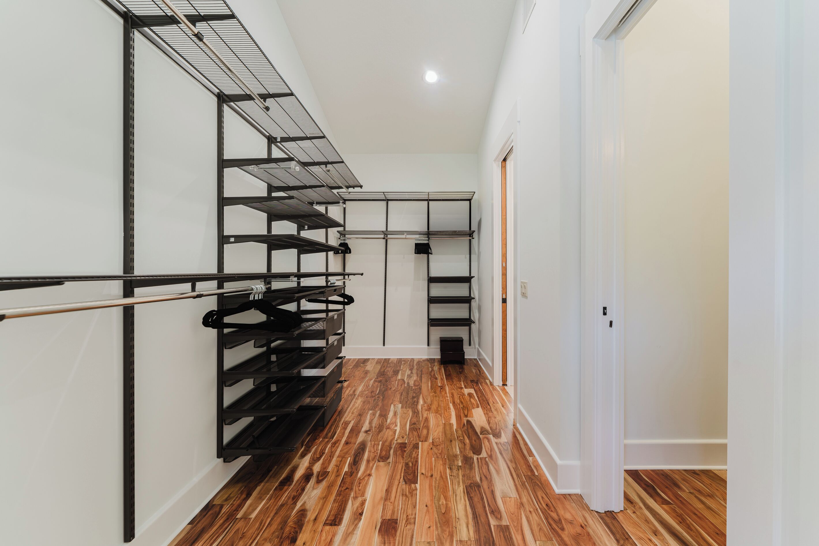A hallway with a wooden floor, metal shelving units, and a white door at the end.
