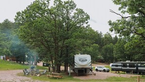 Ein Campingplatz mit einem Wohnmobil der Marke Wolf Pack, Picknicktischen und einem weißen SUV in der Nähe.