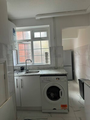 A compact kitchen with a built-in washing machine, a window with frosted glass, and a sink.