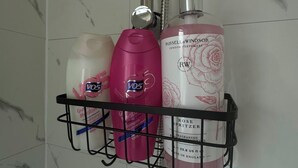 Un estante de baño con artículos de aseo, incluyendo una botella rosa de champú, una botella blanca de acondicionador y una botella grande de perfume.