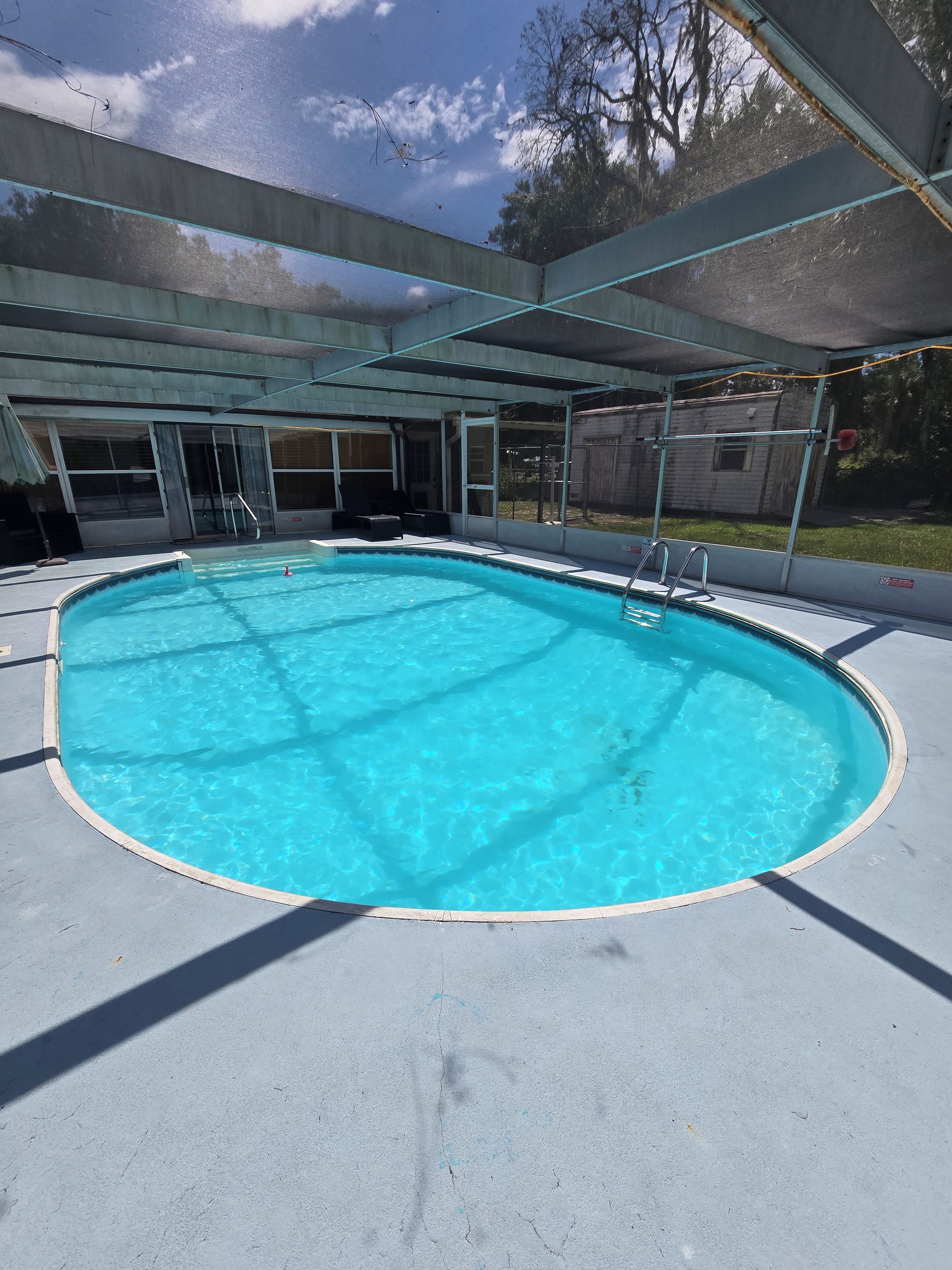 A clear blue swimming pool with a covered deck area, surrounded by a concrete deck.