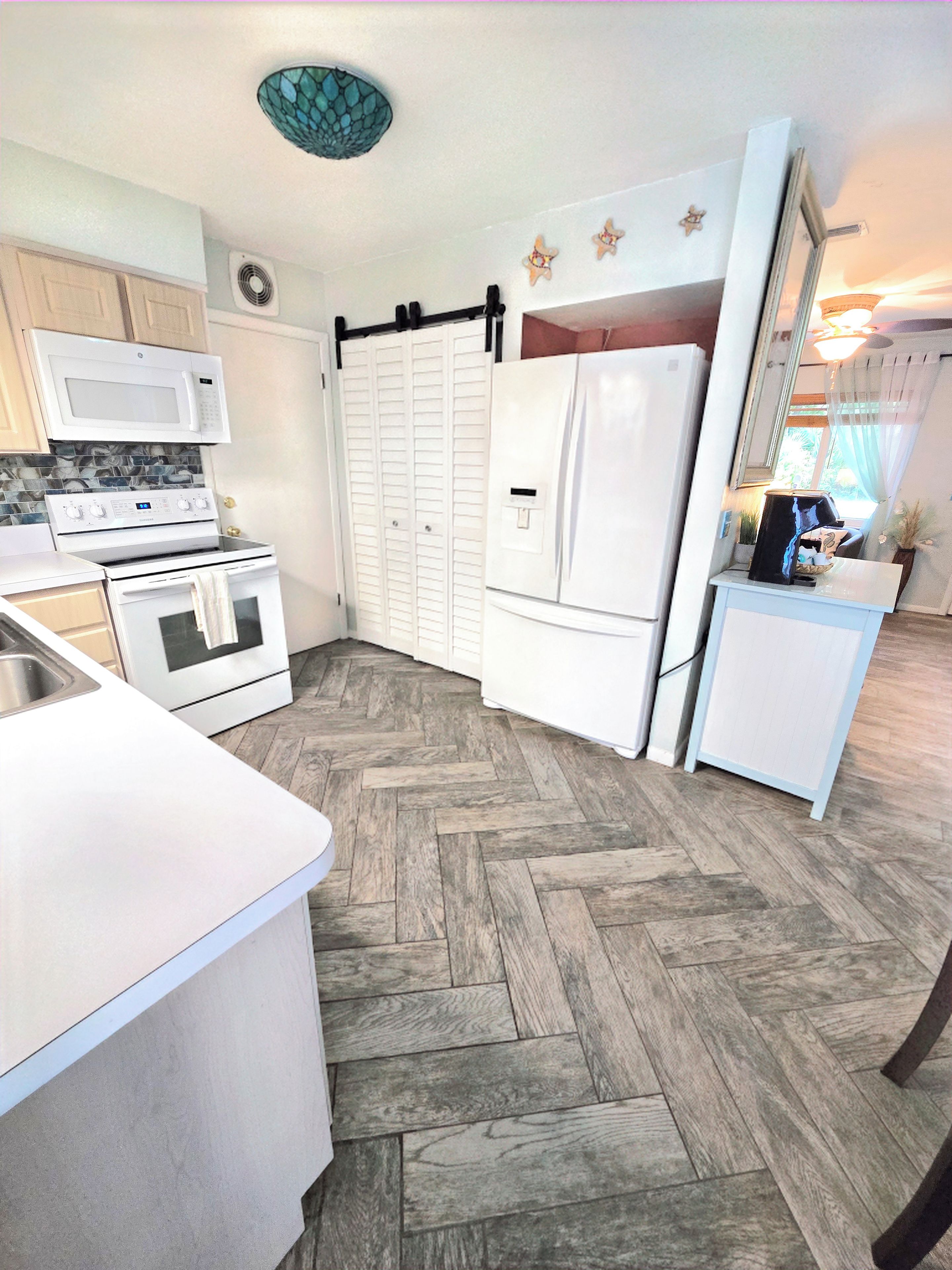 A kitchen with white appliances, a herringbone-patterned floor, and a sliding door closet.