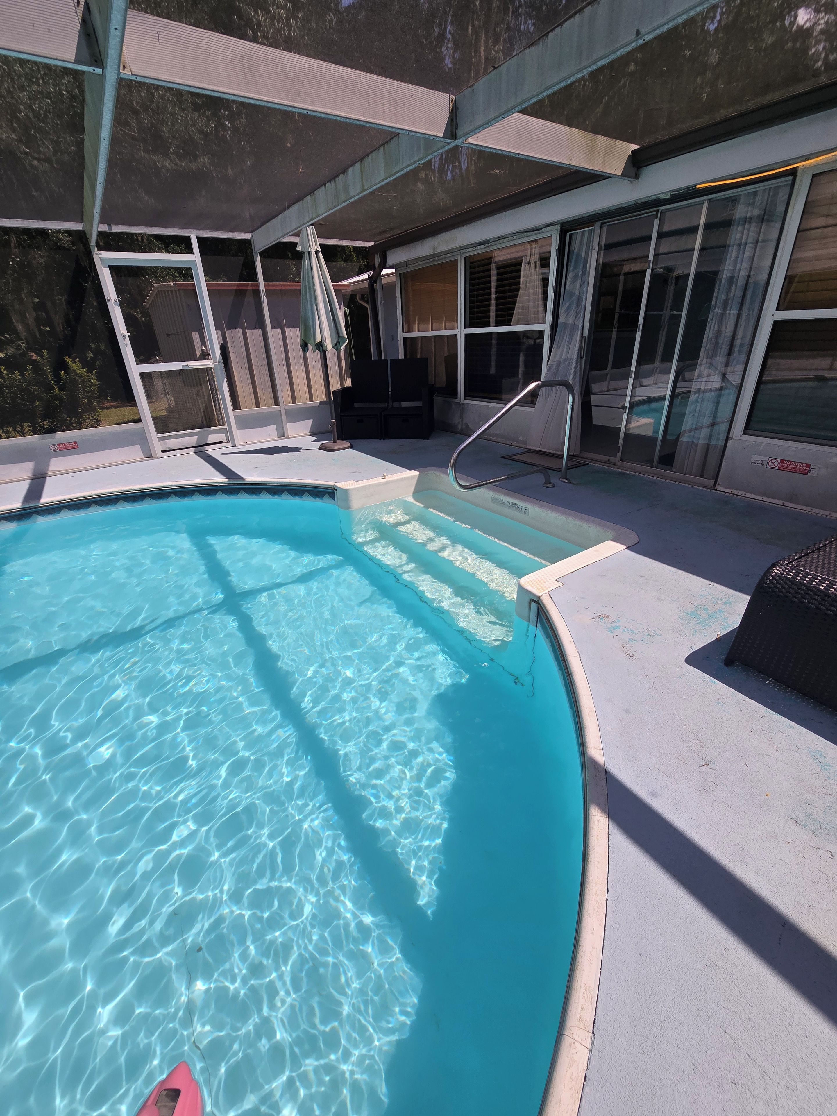 En swimmingpool med ett klart, blått vatten, omgiven av en täckt uteplats med en glasvägg.
