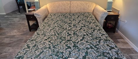 Un dormitorio con colcha estampada de flores, un escritorio con lámpara y vista al océano por la ventana.