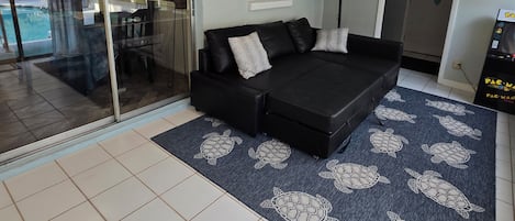 A modern living room with a black sofa, a patterned rug, and a ceiling light fixture.