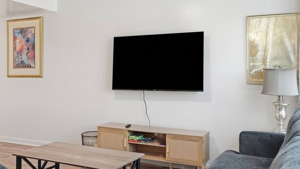 Una sala de estar con televisor montado, un mueble de madera para entretenimiento, un sofá gris y un cuadro abstracto enmarcado.