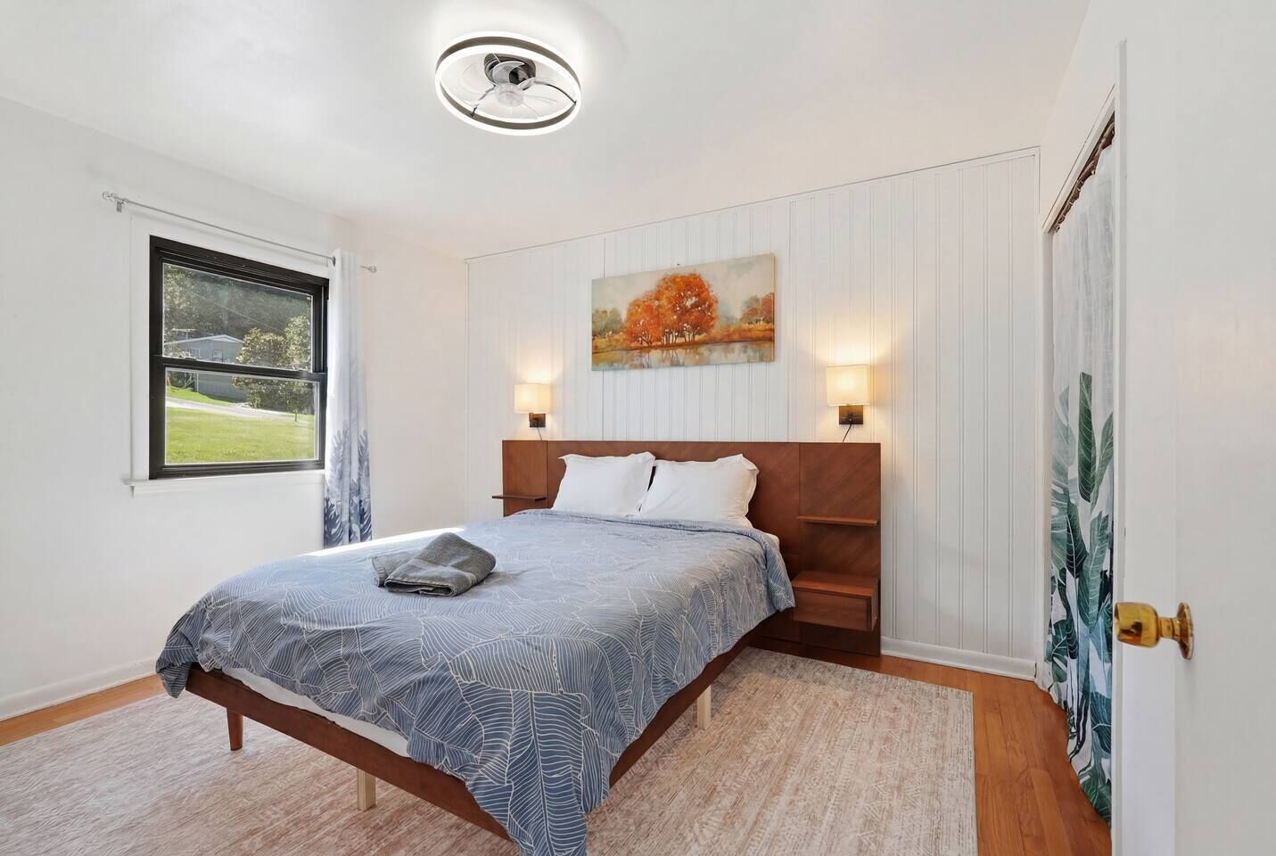 Un dormitorio con cama, un cuadro, una ventana y una puerta.