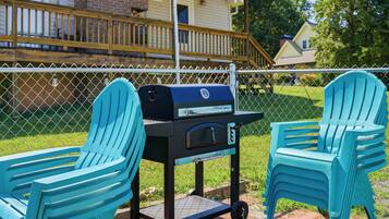 Een terras met een barbecue, twee stoelen en een omheining.