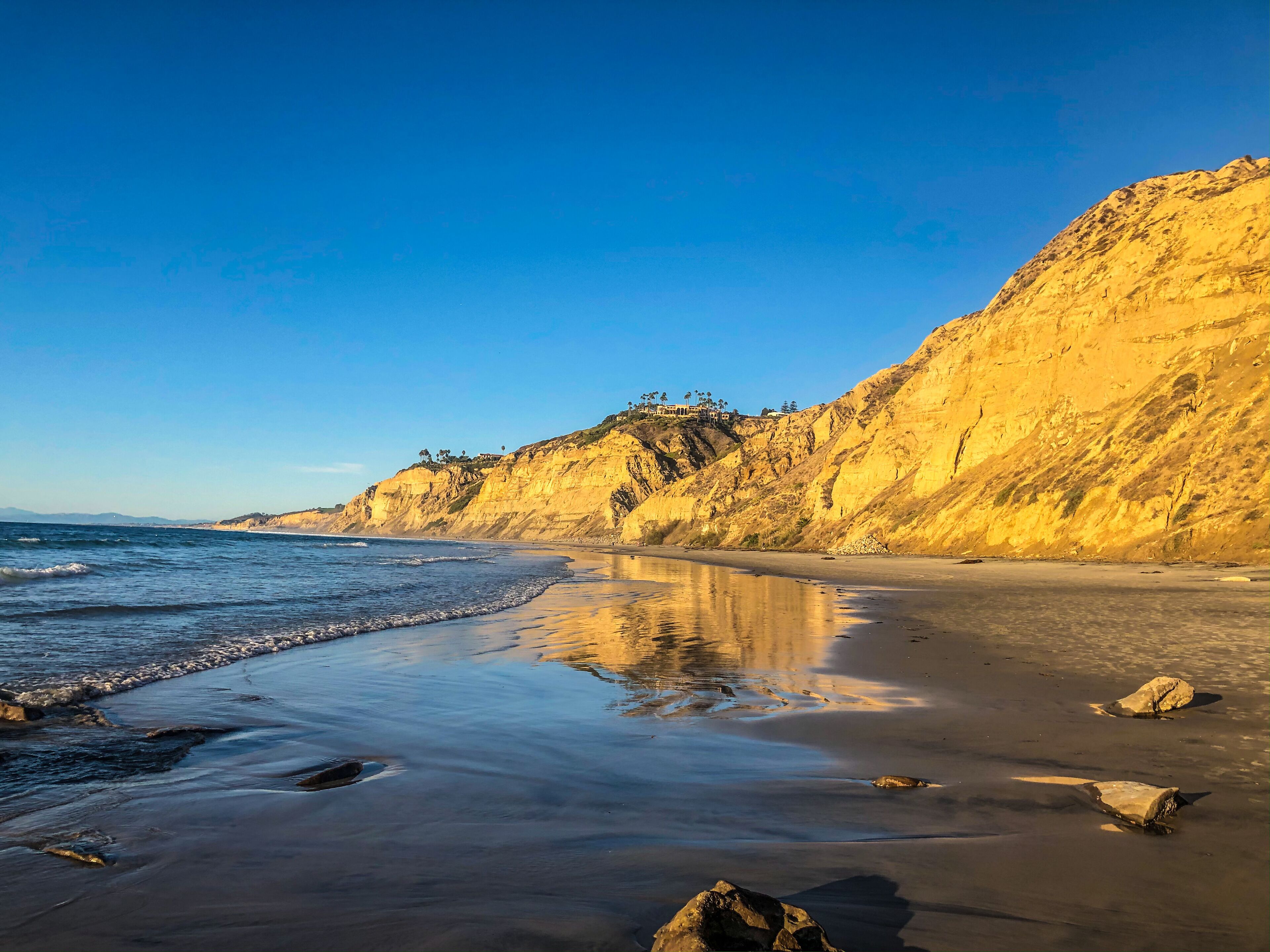 A beach with a clear sky, a sandy shore, and rocky cliffs.