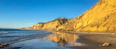 A beach with a clear sky, a sandy shore, and rocky cliffs.
