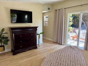 Ein Wohnzimmer mit einer dunkelholznen Kommode, einem Flachbildfernseher, einer beige gestrichenen Wand und Blick auf eine Terrasses.