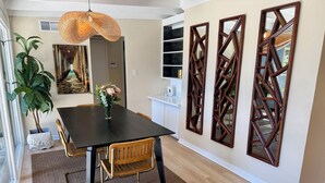 A dining area with a black table, wooden chairs, a woven pendant light, a potted plant, and decorative wall mirrors. - Private retreat w hot tub, sauna & cold plunge steps from La Jolla Shores Beach (San Diego)
