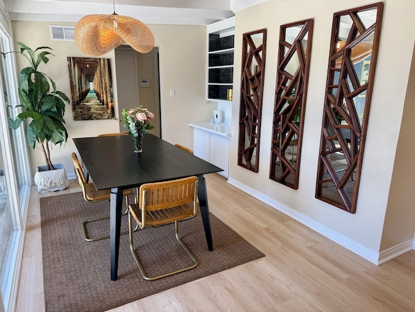 A dining area with a black table, wooden chairs, a woven pendant light, a potted plant, and decorative wall mirrors. - Private retreat w hot tub, sauna & cold plunge steps from La Jolla Shores Beach (San Diego)