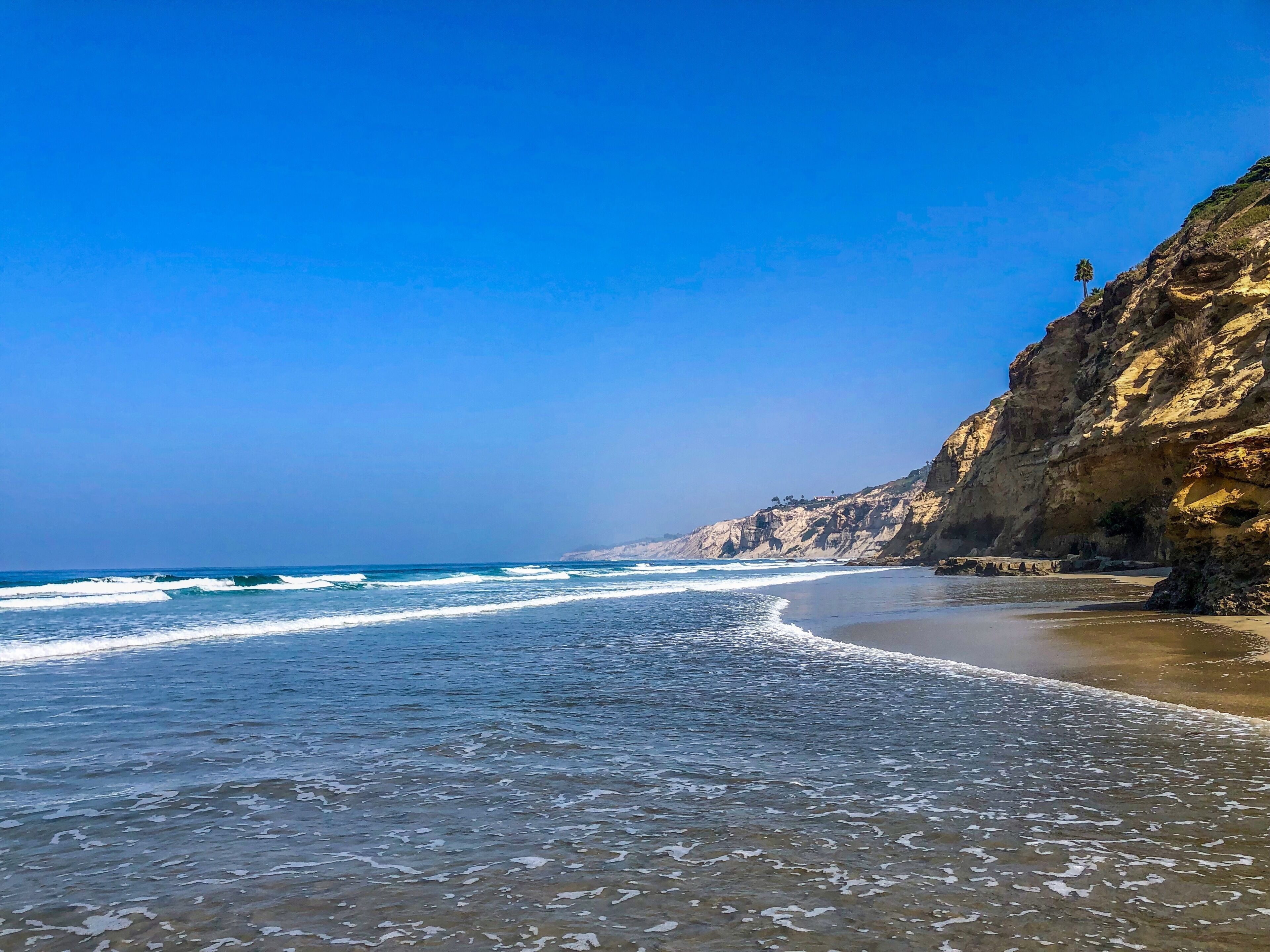 Una spiaggia con cielo sereno, onde e una scogliera rocciosa.