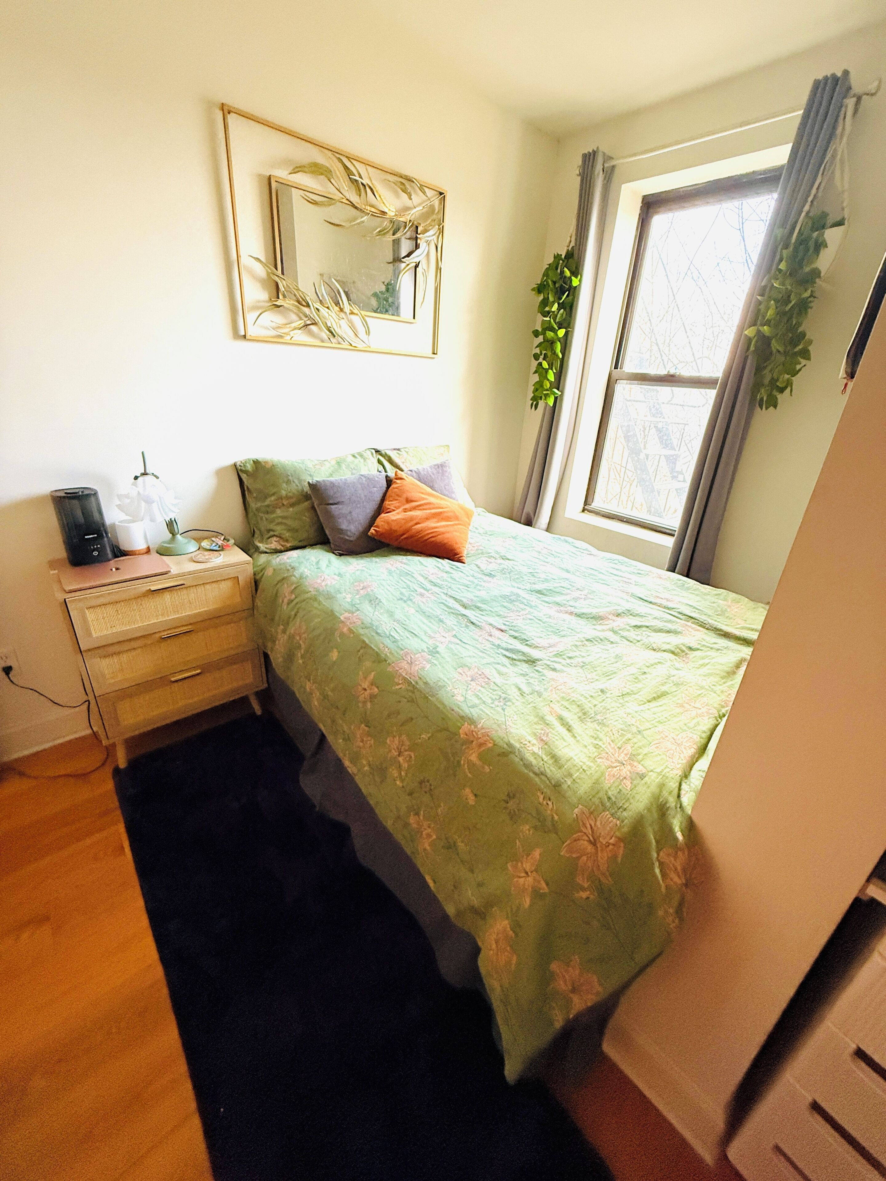 A bedroom with a bed, bedside table, lamp, and a window with curtains.