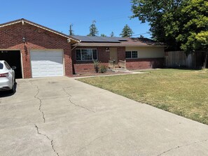 A residential house with a garage, a driveway, and a lawn. - 3-bedroom house in lovely Stockton with cool AC and comfort (Stockton)