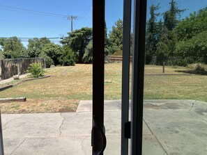 A view through a glass door of a backyard with a lawn, a wooden fence, and trees. - 3-bedroom house in lovely Stockton with cool AC and comfort (Stockton)