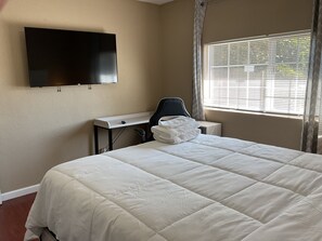 A hotel room with a bed, a desk, a chair, a flat-screen TV mounted on the wall, and a window with blinds. - 3-bedroom house in lovely Stockton with cool AC and comfort (Stockton)