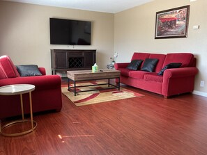 A living room with a red sofa, a red armchair, a coffee table, a flat-screen TV, and a fireplace. - 3-bedroom house in lovely Stockton with cool AC and comfort (Stockton)