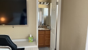 A hotel room with a flat-screen TV, a small table with a box of tissues, a wooden cabinet, and a bathroom visible through an open door. - 3-bedroom house in lovely Stockton with cool AC and comfort (Stockton)