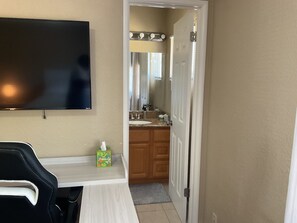 A hotel room with a flat-screen TV, a small table with a box of tissues, a wooden cabinet, and a bathroom visible through an open door. - 3-bedroom house in lovely Stockton with cool AC and comfort (Stockton)
