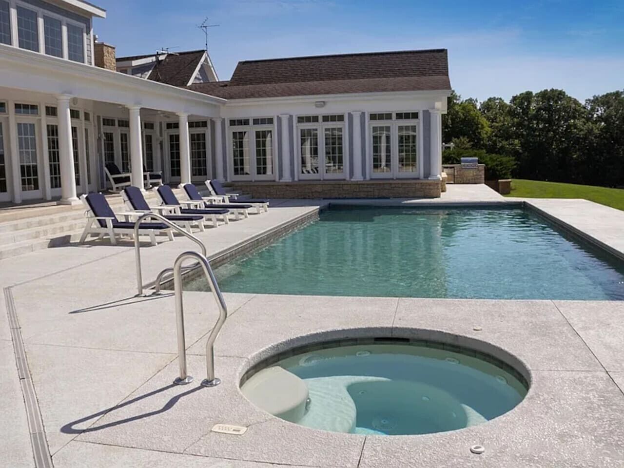 A swimming pool with a hot tub, lounge chairs, and a covered patio area.