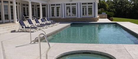 A swimming pool with a hot tub, lounge chairs, and a covered patio area.